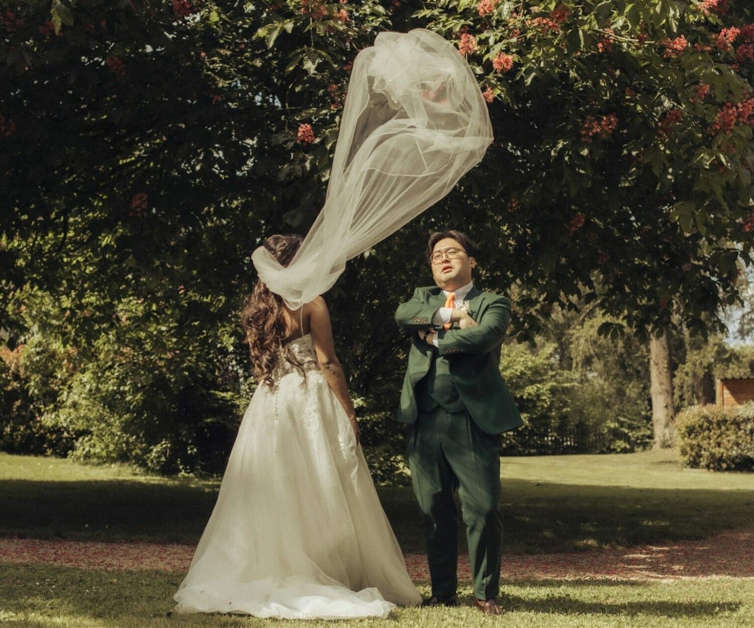 Le marié pose fièrement pendant que le voile de la mariée s’envole