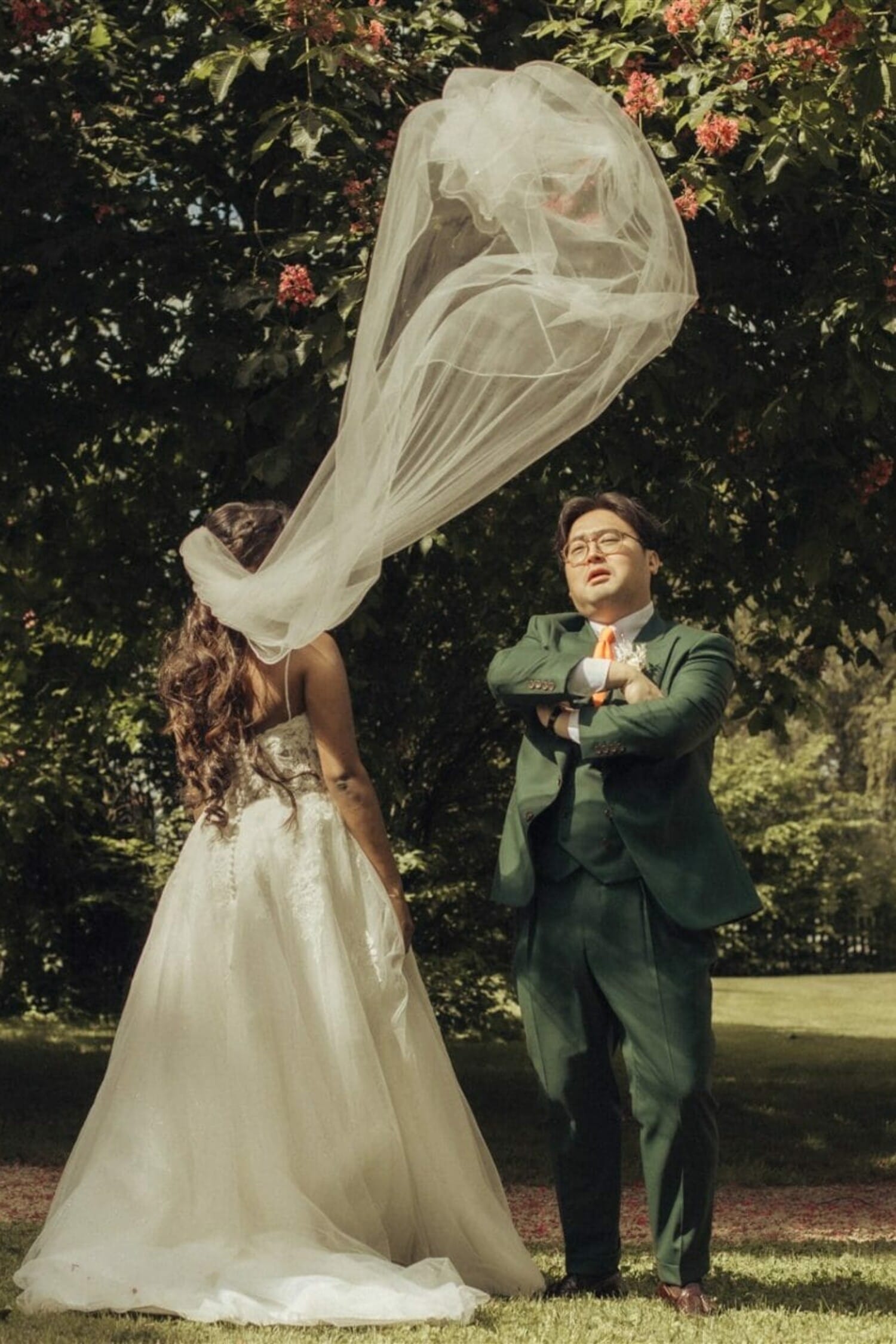 Le marié pose fièrement pendant que le voile de la mariée s’envole