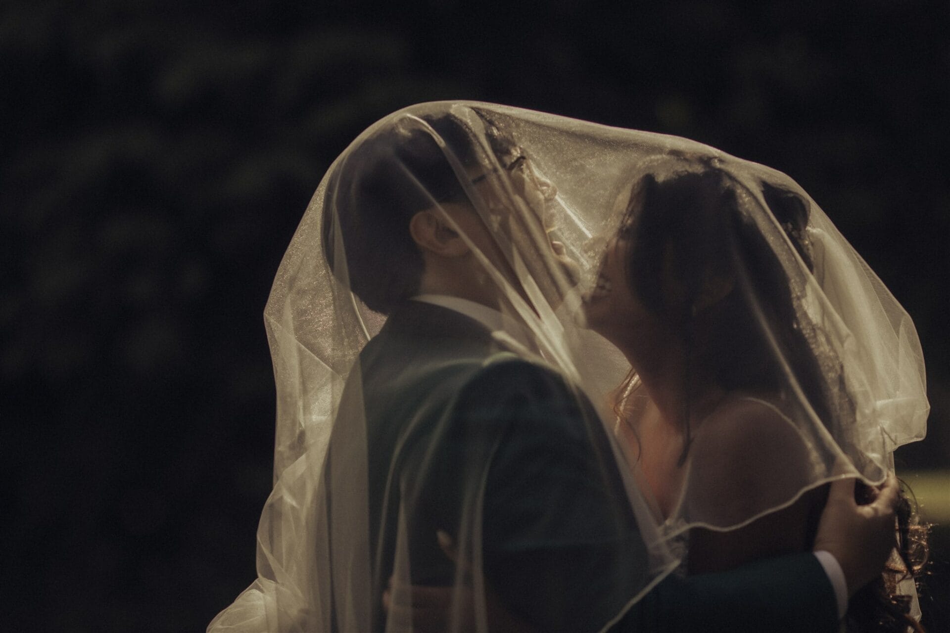 Les mariés s’embrassent sous le voile dans un contre-jour cinématographique par Castille ALMA