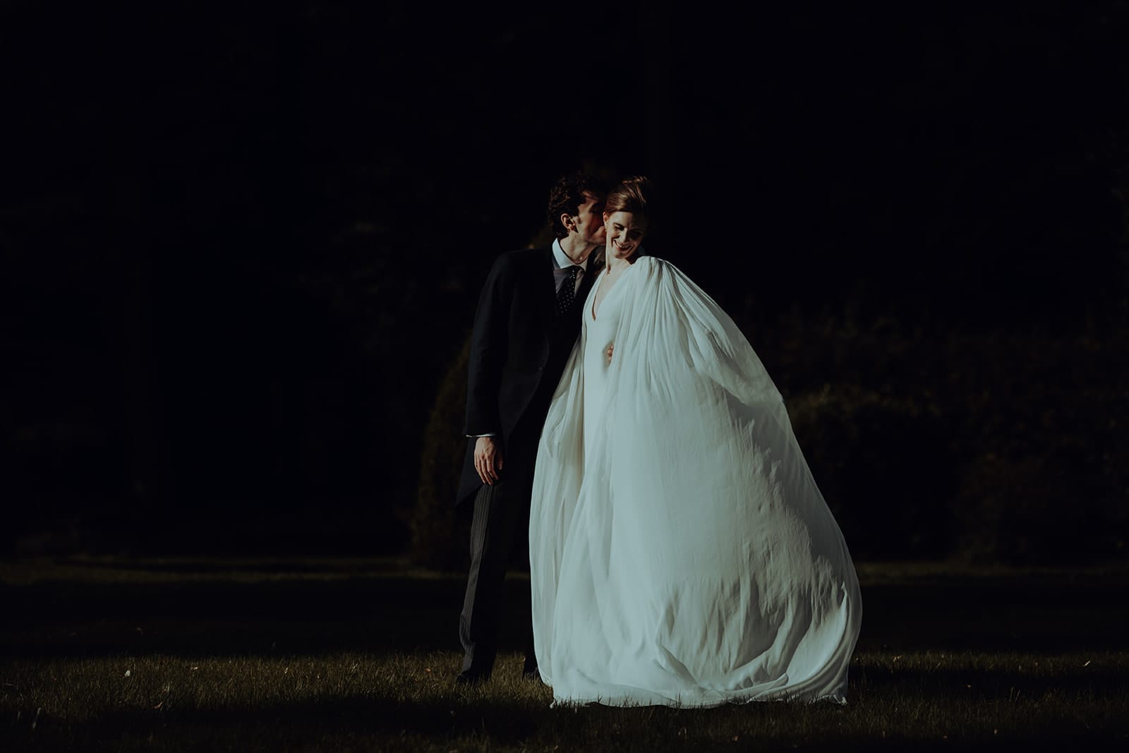 photographe mariage Lyon @castillealma Les mariés s’enlacent tendrement dans une lumière rasante, elle en robe fluide comme sculptée dans le vent, lui en redingote classique, seuls au milieu de l’ombre – par Castille Alma, photographe de mariage à Bangkok et partout en Asie