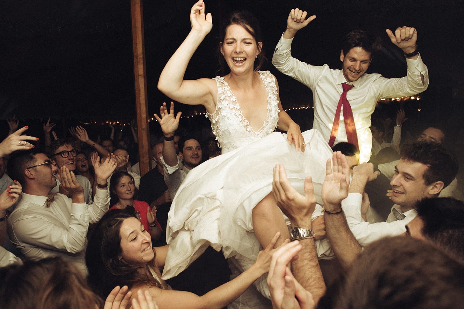 galerie photographe mariage Lyon @castillealma La mariée est portée à bout de bras par ses invité·es en pleine fête, visage rayonnant et bras levé au milieu des cris et des applaudissements – par Castille Alma, photographe de mariage en France