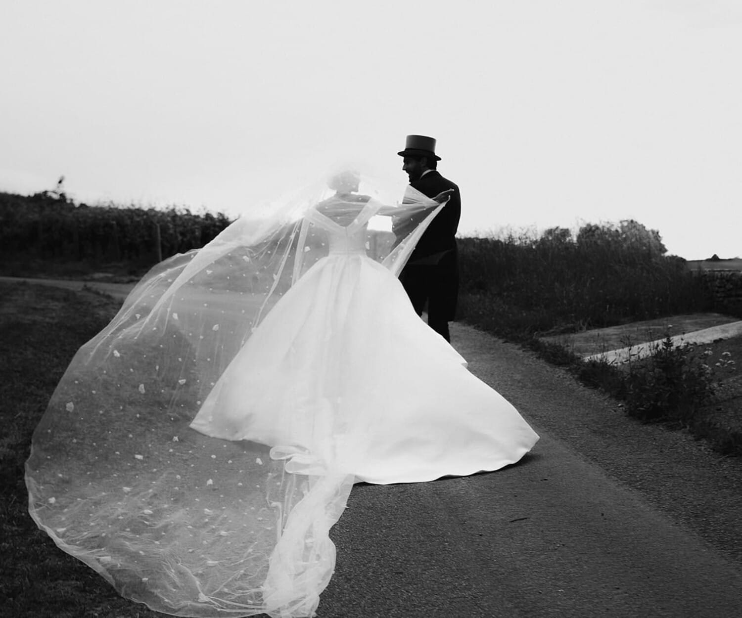 La mariée et son époux marchent dans les vignes du Château de Pierreclos, le voile soulevé par le vent – photo @castillealma