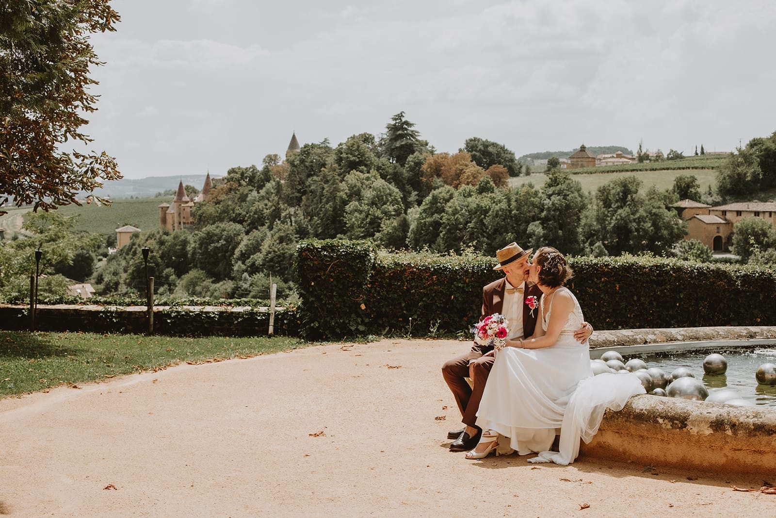 Mariés assis près de la fontaine du Manoir de la Garde à Ville-sur-Jarnioux avec vue sur les collines et châteaux