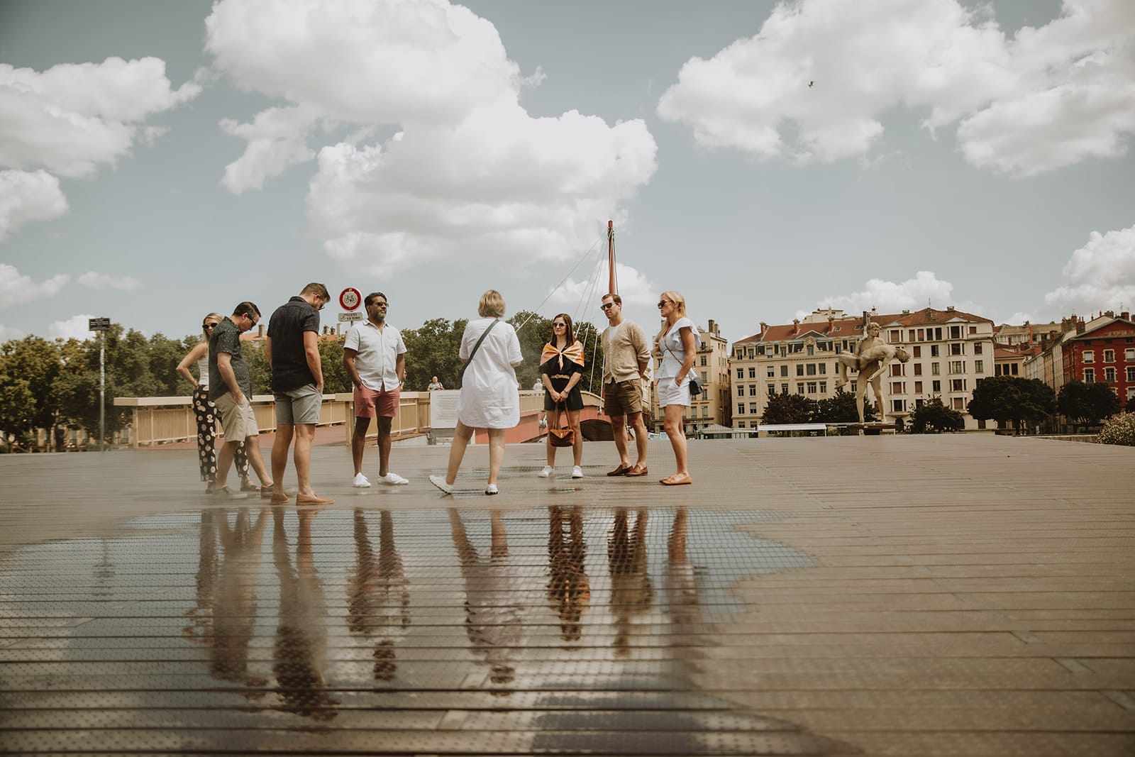 Group of friends standing on a modern square in Lyon, with playful reflections in a puddle