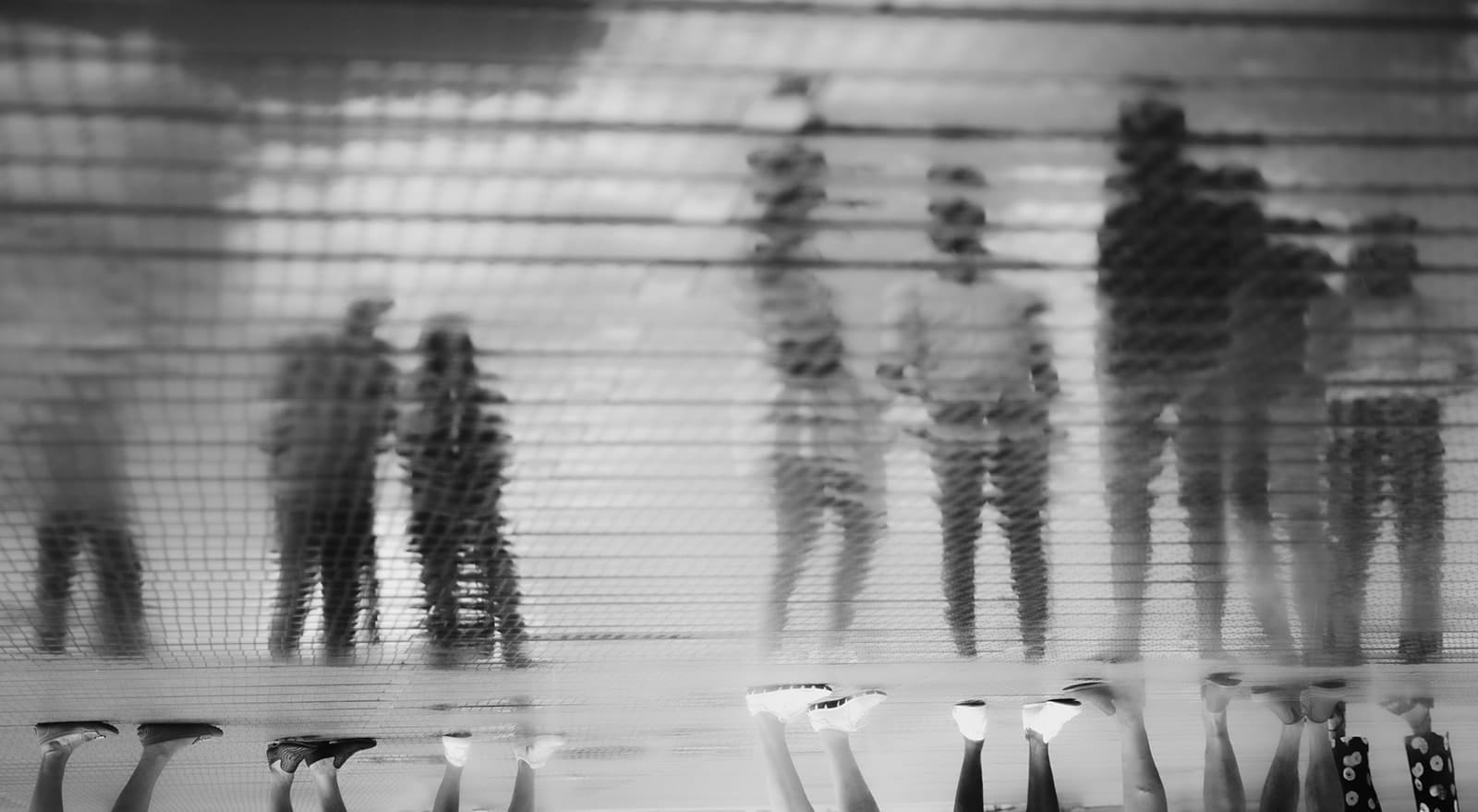 Artistic reflection of a group of people seen through a glass floor, feet below and shadows above