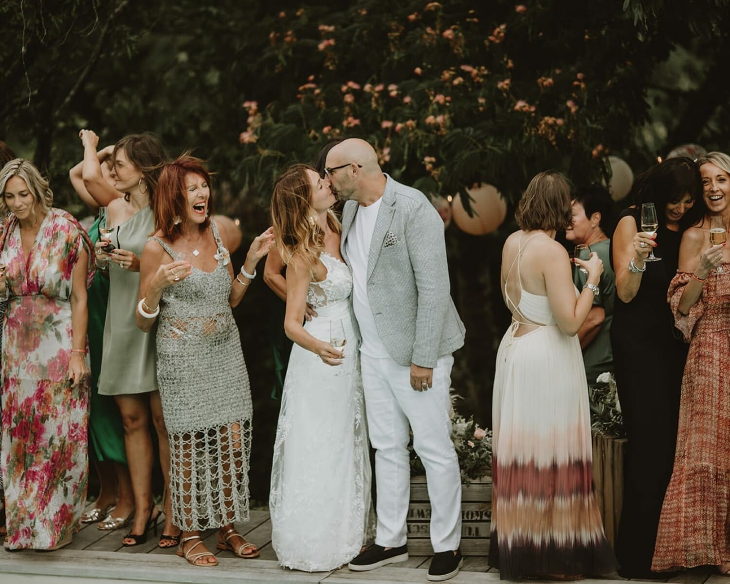 Mariage chic chez soi – couple qui s’embrasse entouré d’invités élégants avec des coupes de champagne