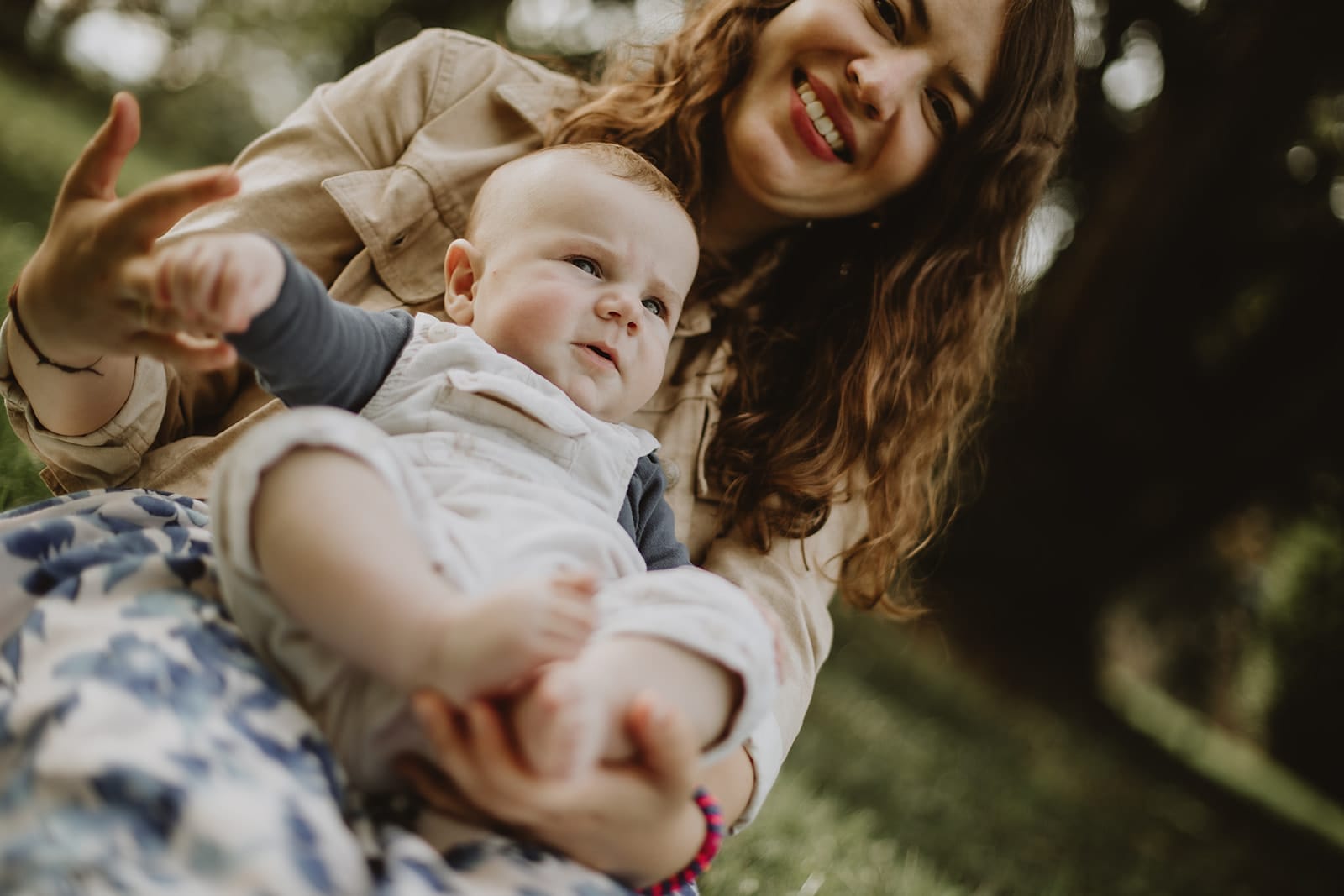 Une mère souriante tient son bébé sur l'herbe, pleine d'affection.