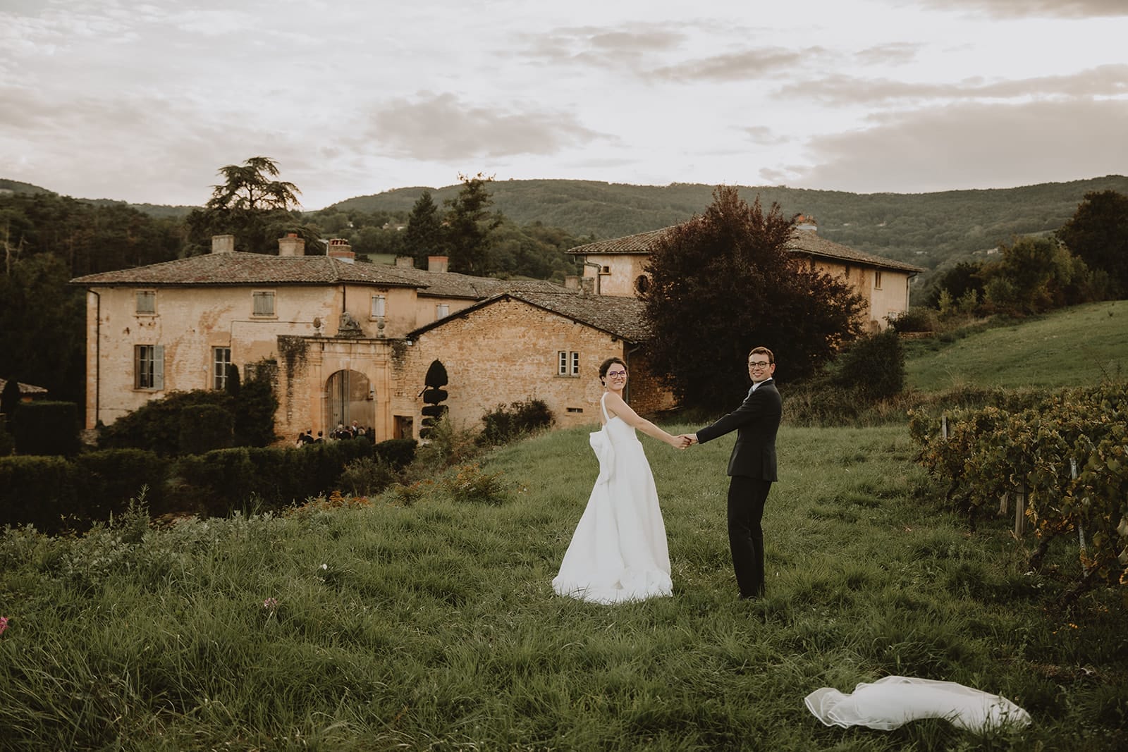 Un couple heureux se tient la main devant un manoir pittoresque.