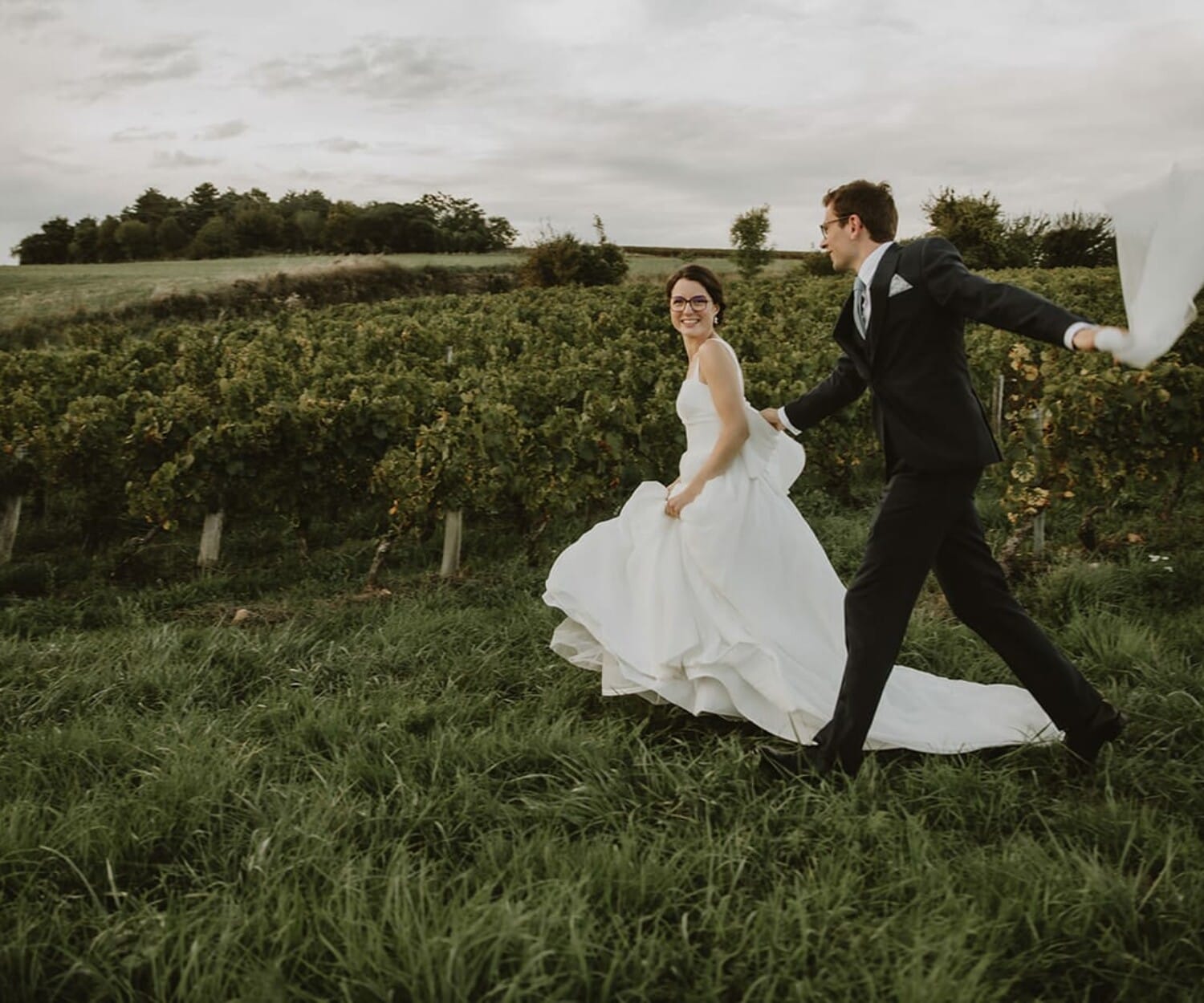 Un couple joyeux dans un vignoble à Lyon, vêtus de leurs habits de mariage.