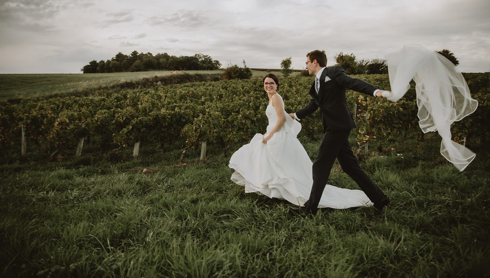Un couple joyeux dans un vignoble à Lyon, vêtus de leurs habits de mariage.