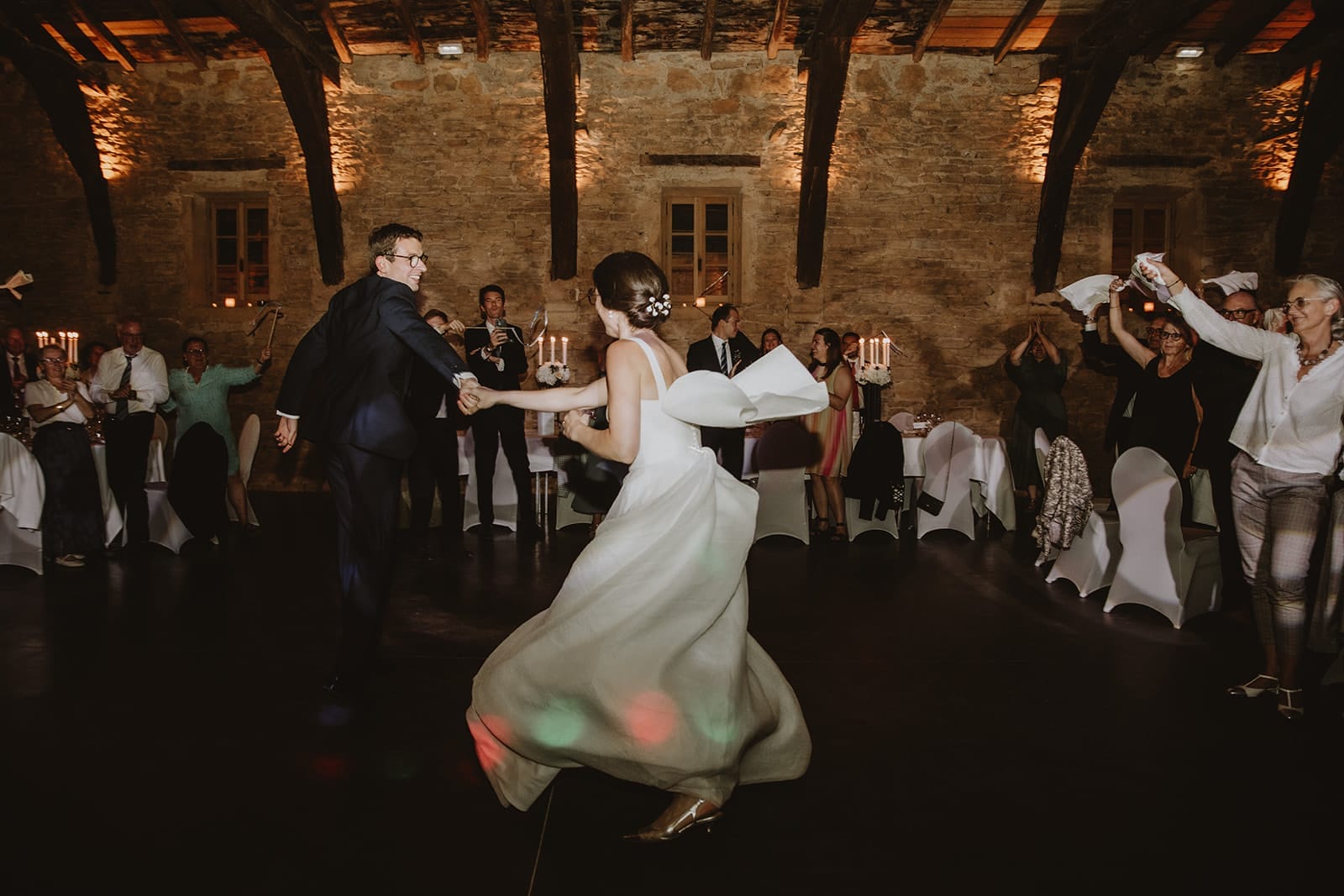 Un couple danse joyeusement sous les lumières tamisées d'un manoir.