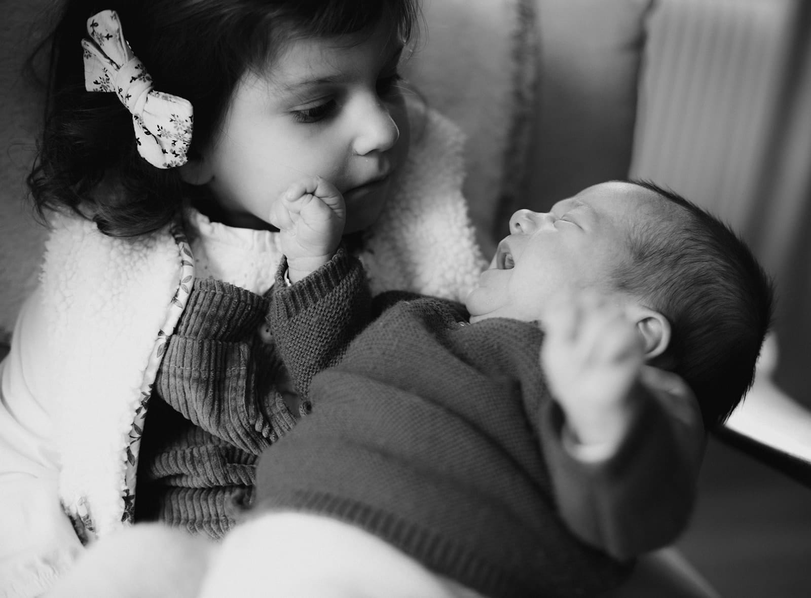 Une grande sœur observe tendrement son petit frère qui rit.
