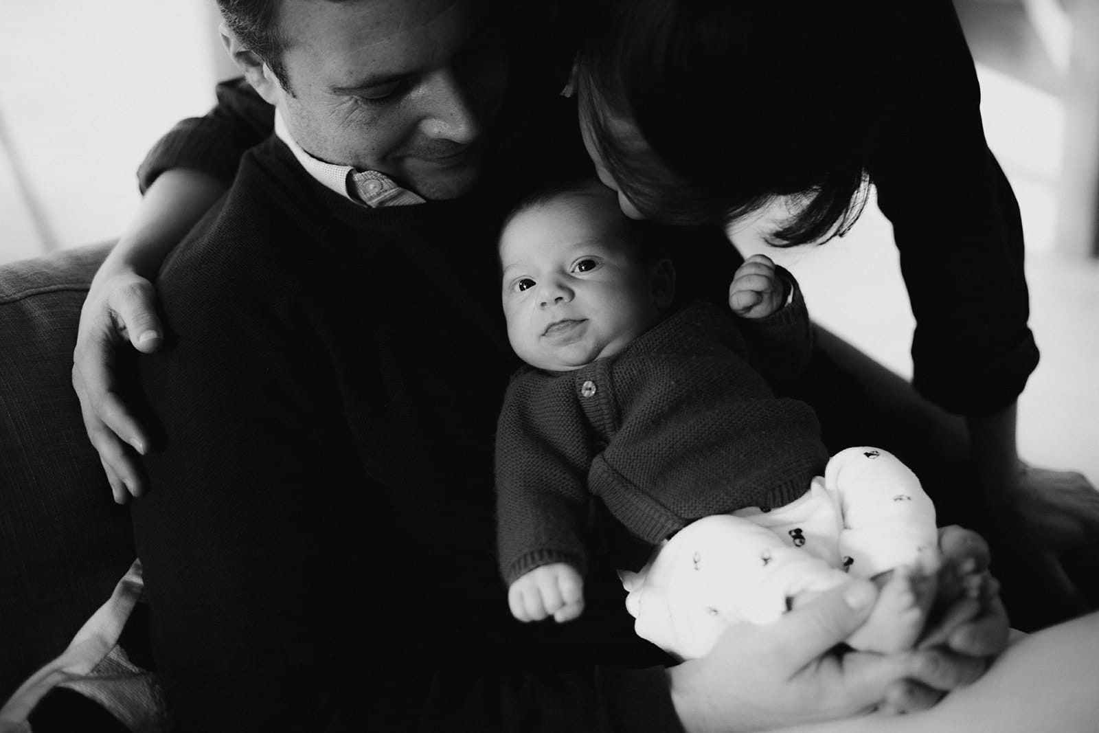 Un père souriant tient son bébé dans ses bras, entouré d'amour.