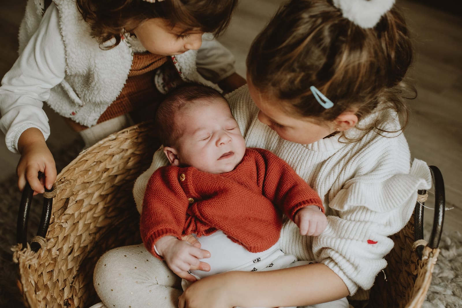 Un nouveau-né paisible entouré de ses sœurs dans un panier en osier.