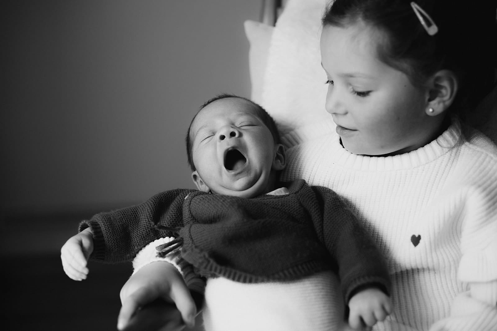 Un bébé qui bâille dans les bras de sa grande sœur à Lyon.